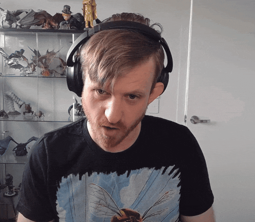 a man wearing headphones stands in front of a shelf full of figurines