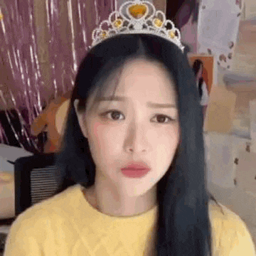 a woman wearing a yellow sweater and a tiara is making a funny face .
