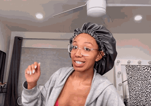 a woman wearing glasses and a satin bonnet is standing in front of a ceiling fan