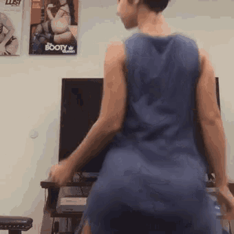 a man in a blue tank top is dancing in front of a tv with a booty magazine on the wall behind him