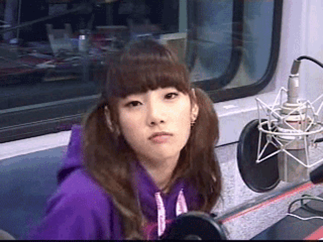 a young woman in a purple hoodie stands in front of a microphone