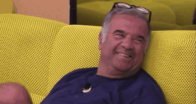 a man wearing glasses is sitting on a yellow couch