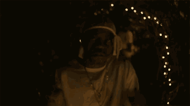 a man in a white shirt is standing in the dark with a string of lights behind him