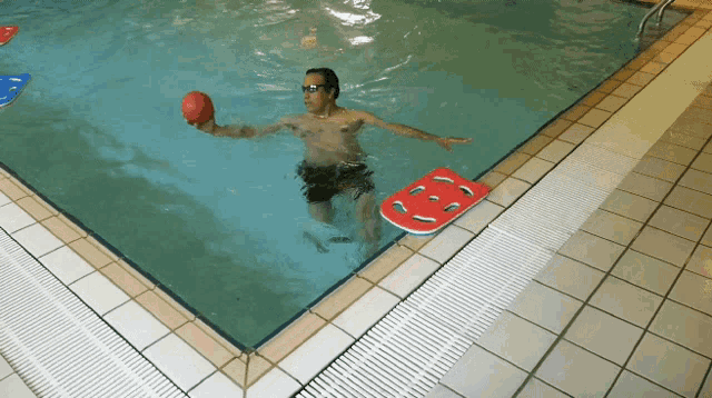 a man in a swimming pool holds a red ball in his hand