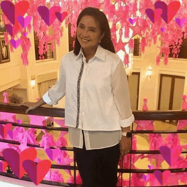 a woman is standing on a balcony with pink hearts hanging from the ceiling behind her .