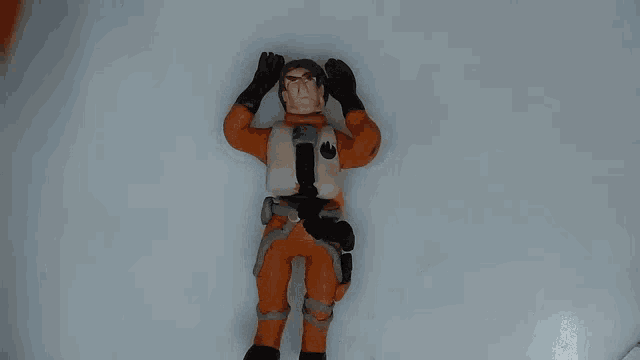 a toy figure of a man in an orange suit with a star wars logo on his chest