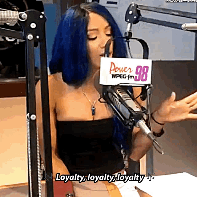 a woman with blue hair speaking into a microphone with a sign that says power 98