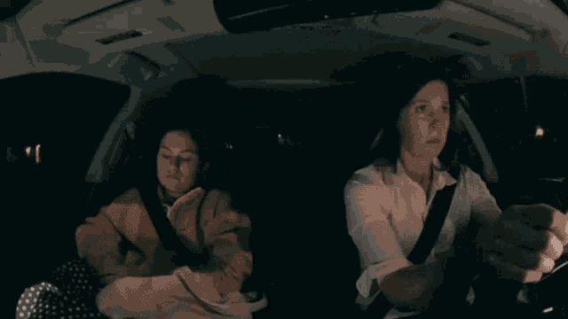 two women are sitting in a car at night and one is driving