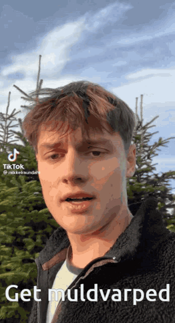 a young man stands in front of a christmas tree with the caption get muldvarped