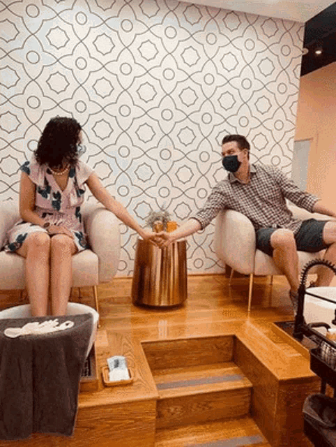 a man and a woman are sitting in chairs holding hands in a salon .