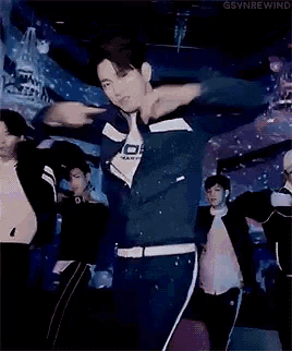 a group of men are dancing on a stage and one of them is wearing a blue shirt with the letter s on it .