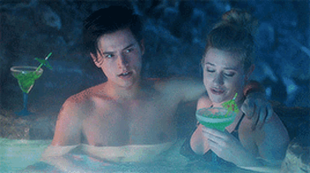 a man and a woman are sitting in a hot tub with a drink .