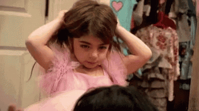 a little girl in a pink dress is putting her hair in a bun .