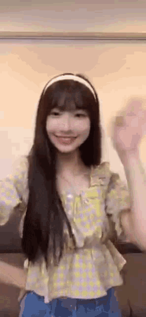 a girl with long hair is wearing a yellow shirt and a headband and waving .