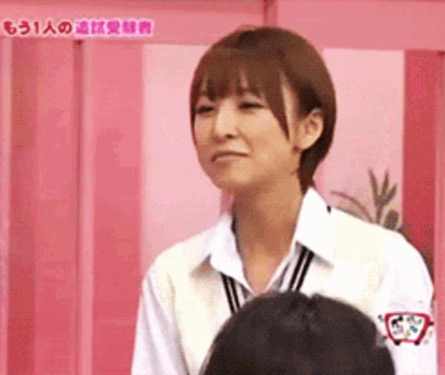 a woman in a white shirt is standing in front of a pink wall with chinese writing on it ..