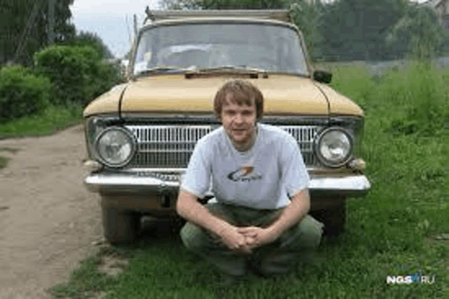 a man is kneeling in front of a yellow car in a field .