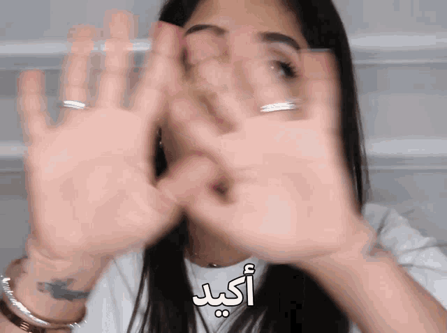 a woman covering her face with her hands with arabic writing on the bottom right