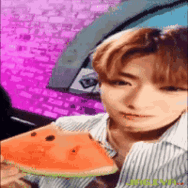 a young man is holding a slice of watermelon in his hand