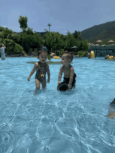 a boy and a girl are playing in a pool with a sign that says ji than tai on it