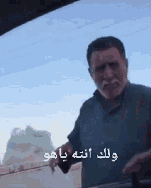 a man with a beard is standing in front of a car window and talking in arabic .
