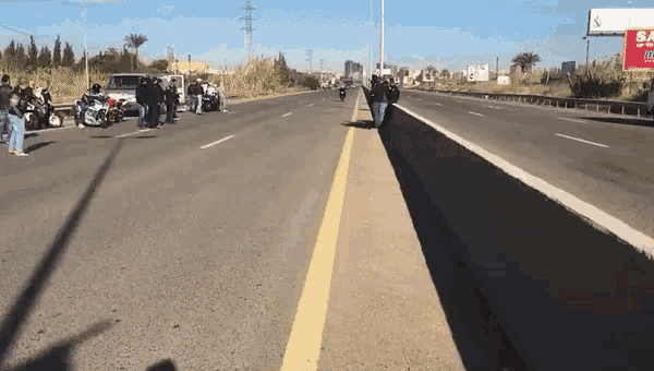 a group of people standing on the side of a highway in front of a billboard