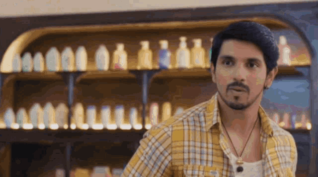a man in a yellow plaid shirt is standing in front of a shelf full of bottles