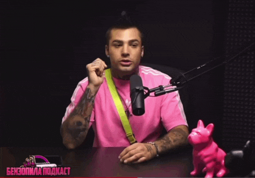 a man in a pink shirt is sitting in front of a microphone with the word podcast written on the bottom