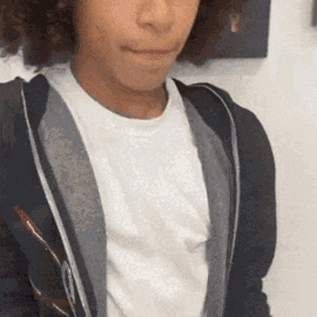 a young boy with curly hair is wearing a white shirt and a black hoodie .