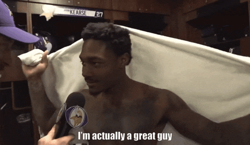 a shirtless man is being interviewed in a locker room by a man wearing a vikings hat