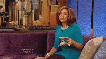 wendy williams is sitting on a couch holding a mug of coffee .