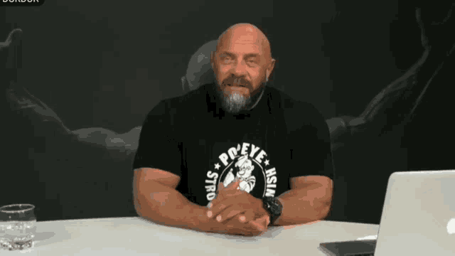 a bald man with a beard wearing a black shirt that says " believe strong "
