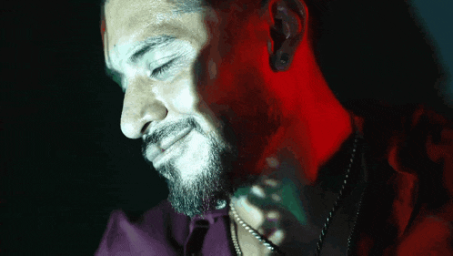 a close up of a man 's face with a beard and a necklace .