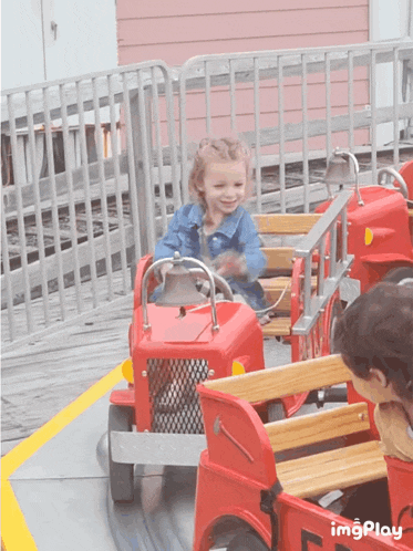 a little girl is riding a red toy fire truck on a roller coaster