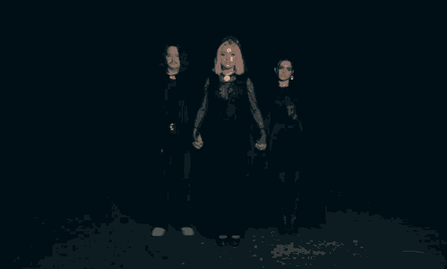 a woman in a black dress stands between two men in black capes