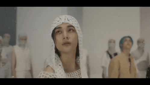 a woman wearing a crocheted head scarf is standing in front of a group of people in white clothes .