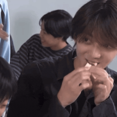 a man in a black jacket is eating a piece of food while sitting at a table with other people .