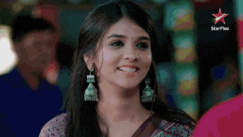 a woman wearing earrings is smiling in front of a star plus sign .
