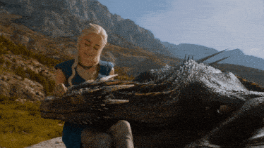 a woman sitting next to a large dragon in the mountains