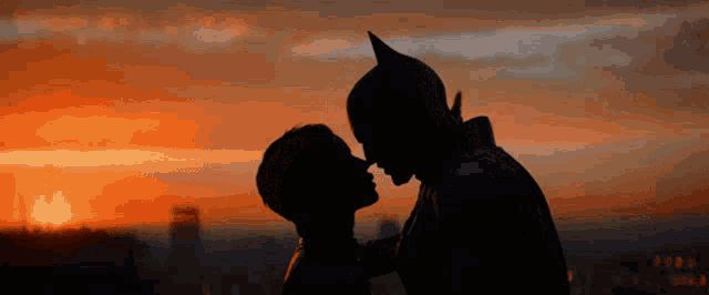 a silhouette of batman and catwoman kissing at sunset .