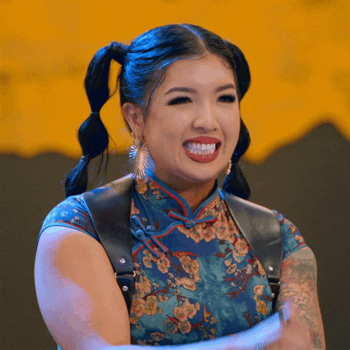 a woman with pigtails is smiling and wearing a blue floral dress
