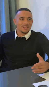 a man in a black sweater and white shirt is sitting at a table and smiling