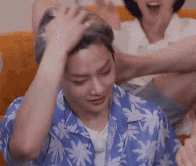 a man in a blue shirt with palm trees on it is sitting on a couch and holding his head .