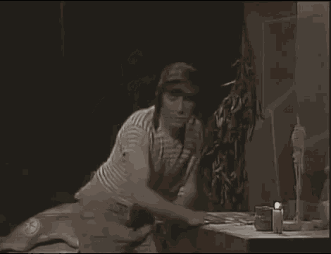 a man in a striped shirt is sitting at a table with a candle in a dark room .