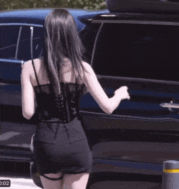 a woman in a black dress is standing in front of a black suv