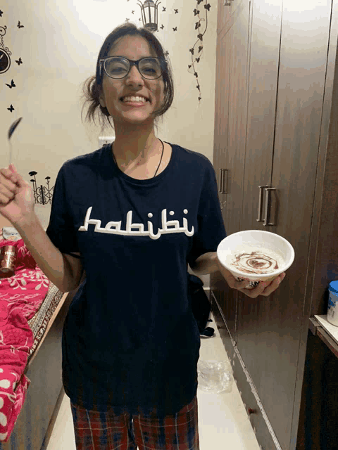 a woman wearing a t-shirt that says habibi is holding a bowl of food