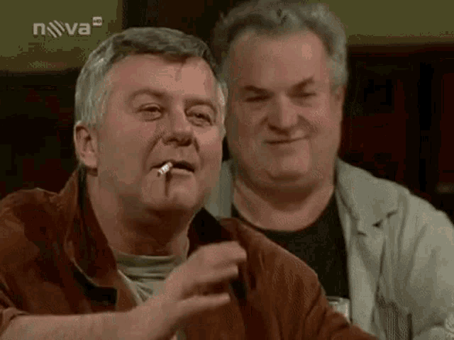 a man is smoking a cigarette while sitting at a table with another man .