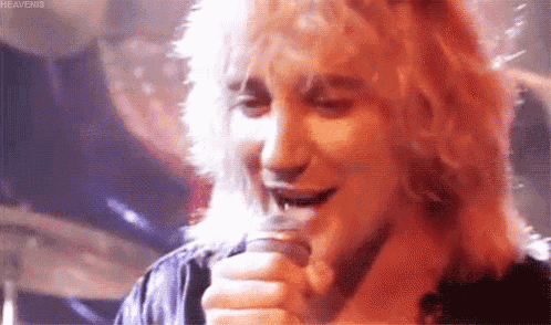 a man with long blonde hair is singing into a microphone .