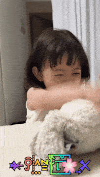a little girl is playing with a stuffed animal with the letter x on the bottom right