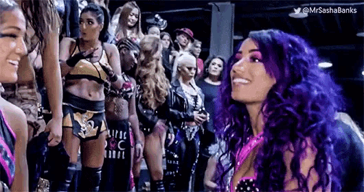 a woman with purple hair is standing in front of a group of women .