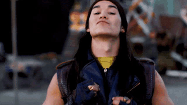 a man with long hair wearing a purple vest and a yellow shirt